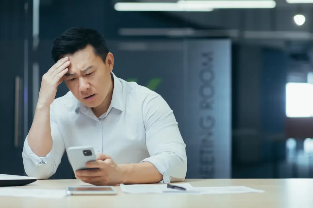 Upset asian businessman working in office, reading bad news on phone, man depressed at work.